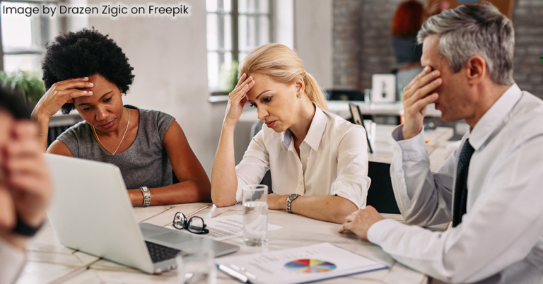 frustrated professionals gathered around a table with computers